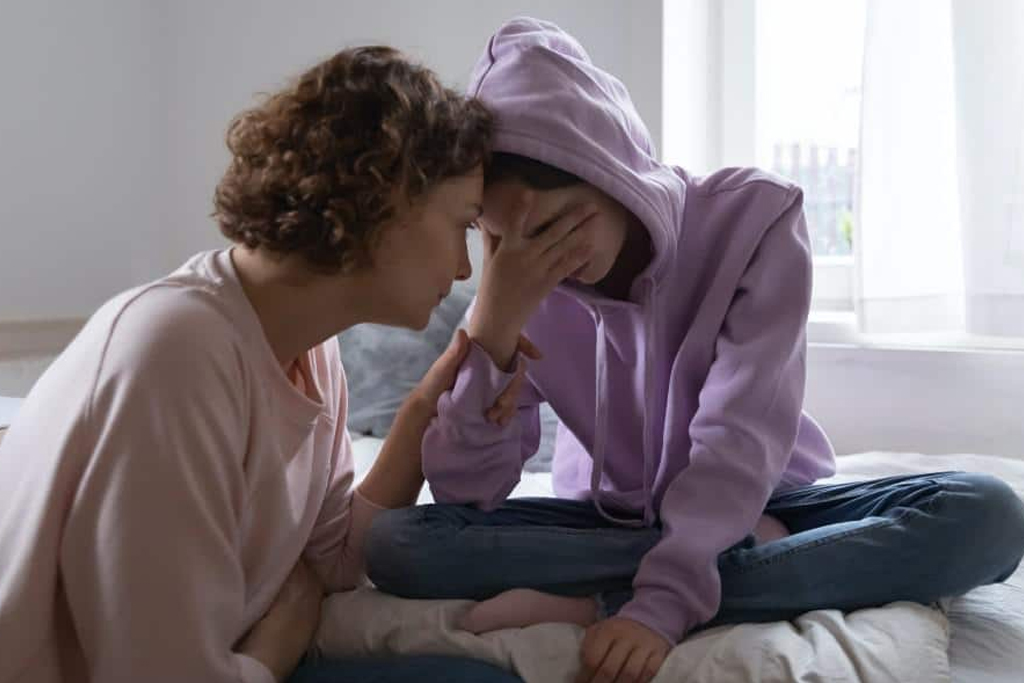 mother and her teen sitting with their heads together as the teen struggles with thoughts of self-harm